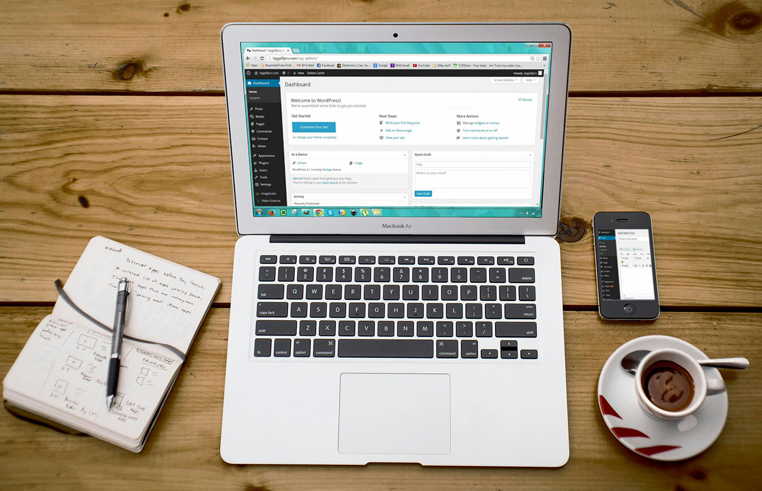 A laptop on a wodden desk displaying the WordPress dashboard. Beside the laptop is a cellphone, coffee cup, and notebook.